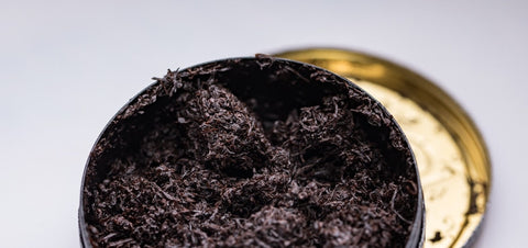 Open tobacco tin with tobacco leaves on a light background