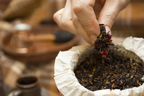 Hand holding dried tea leaves over a container of tea, with a blurred background