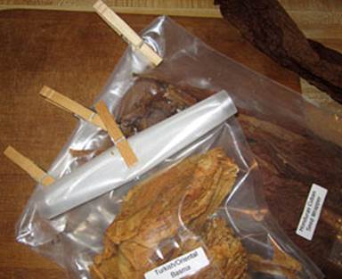 Two clear plastic bags filled with tobacco leaves are sealed with wooden clothespins.